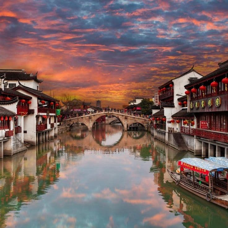 Qibao Ancient Town waterfront with canal boats, stone arch bridges and red lanterns